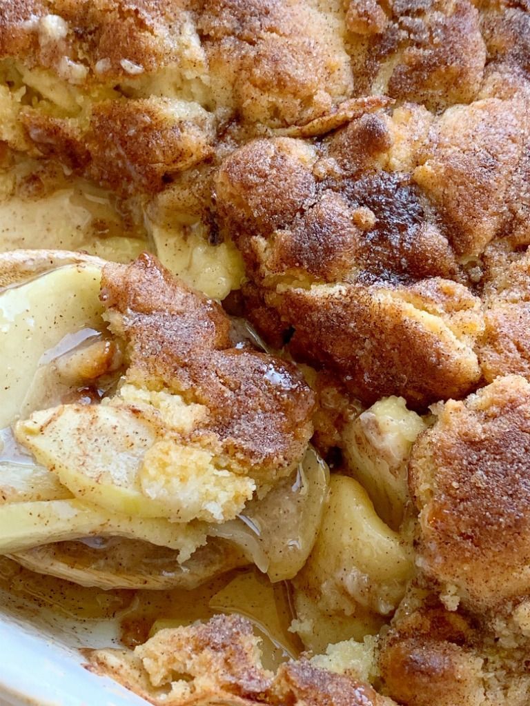 Apple cobbler with golden-brown, cinnamon-sugar topping and baked apples visible beneath.