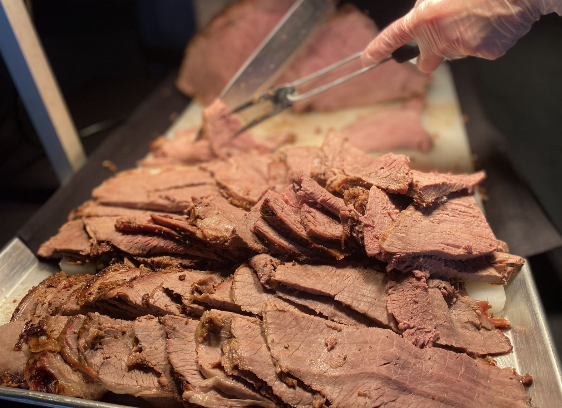 Sliced roast beef on a tray, being served with tongs.