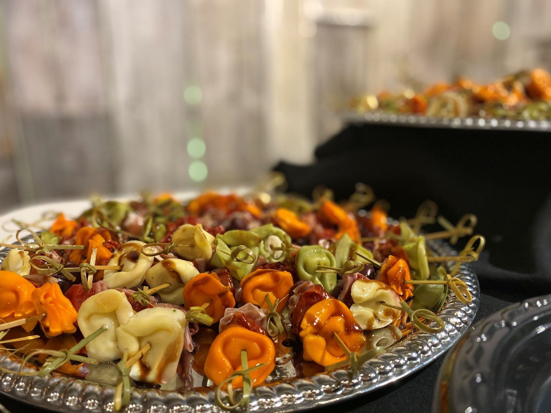 Tortellini skewers on silver platter, with a blurred background.