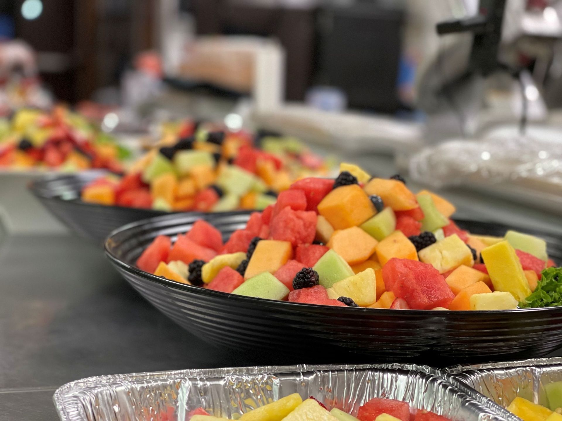 Fruit salad in black bowls and foil containers on a buffet table.