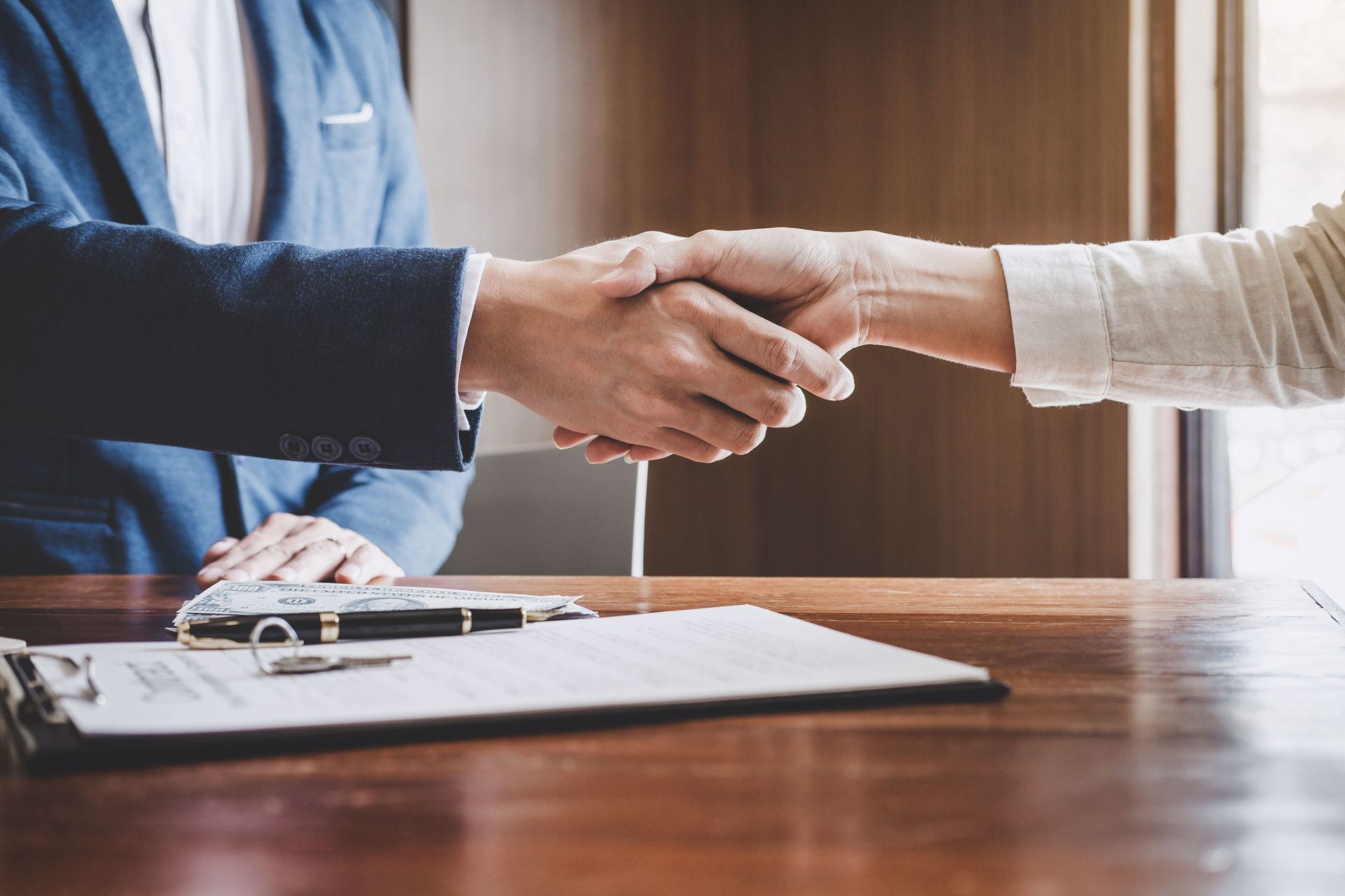 Two people shaking hands over a contract on a wooden desk.