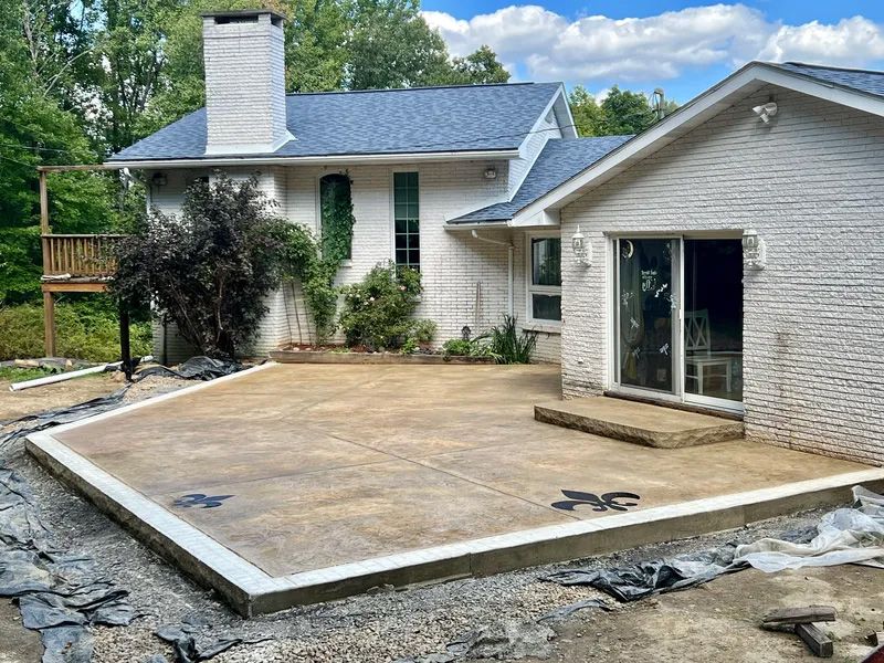 Concrete patio being constructed next to a white brick house with a sliding glass door.