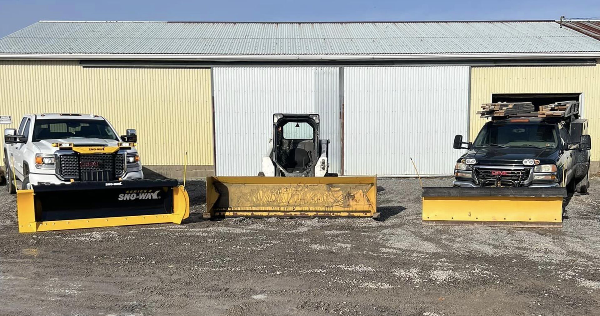 Three snowplow vehicles lined up in front of a building.