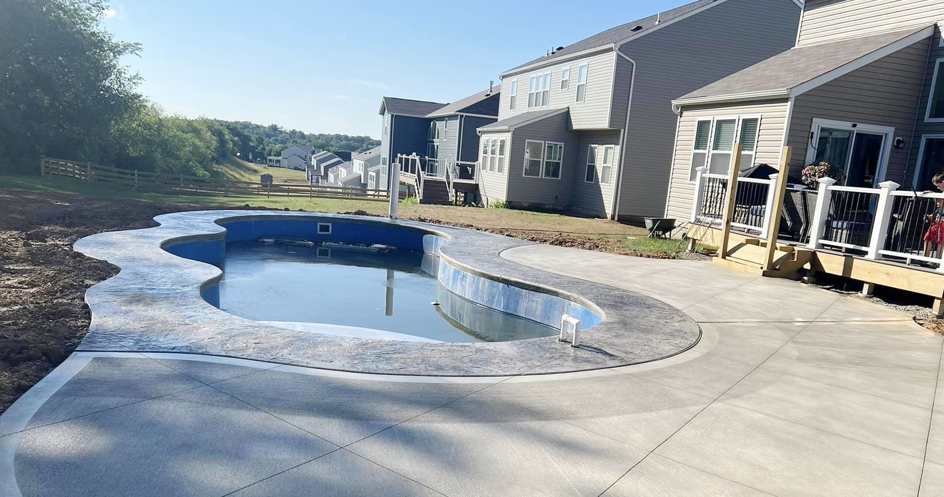 Pool and patio construction at a house. The pool is empty and surrounded by concrete. Houses in the background.