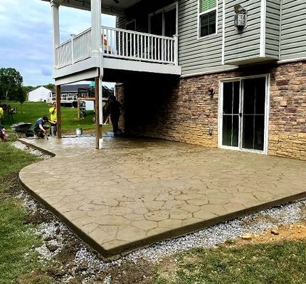 Stamped concrete patio under a second-story deck, adjacent to a house with a sliding glass door.