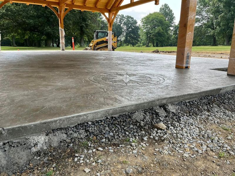 Newly poured concrete under a wooden pavilion with a small bulldozer in the background.