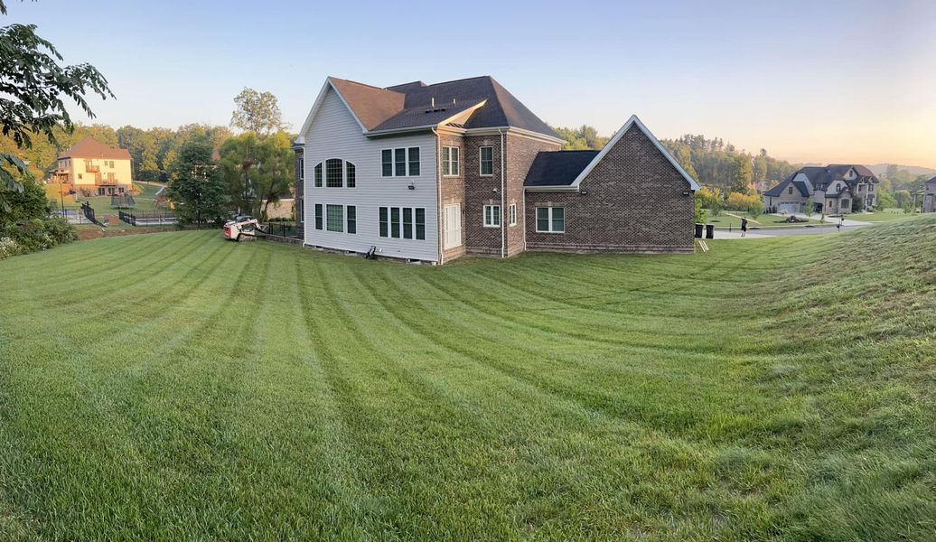 Large house with mowed lawn, trees, and a sky at dawn or dusk.