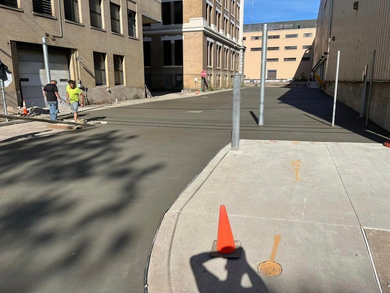 Construction workers smoothing wet concrete in an alleyway with buildings on either side.