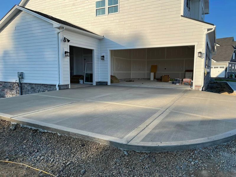 Newly poured concrete driveway in front of a light-colored house with an open garage.