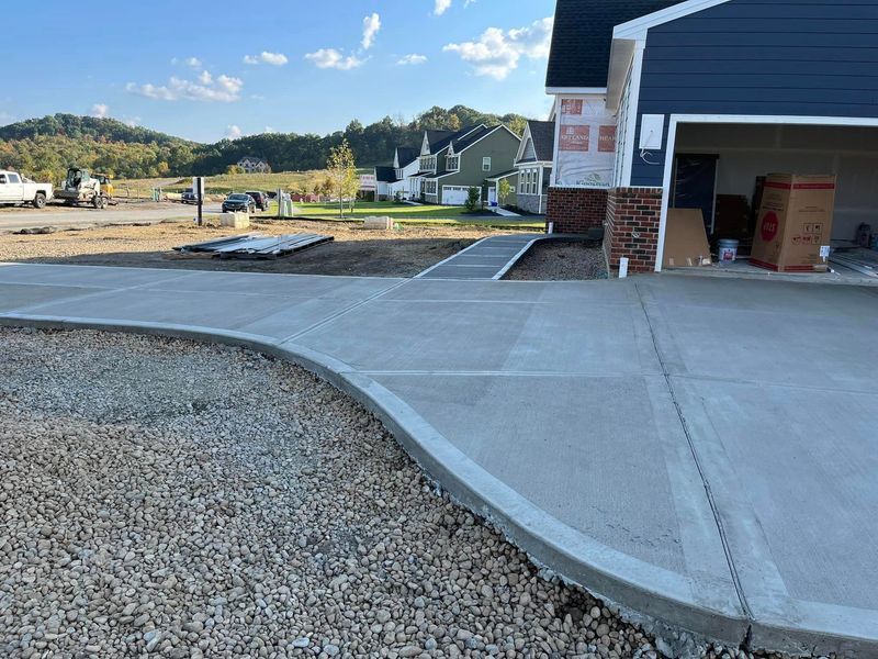 Newly poured concrete driveway curving toward a garage under construction, gravel on the side, houses in the distance.