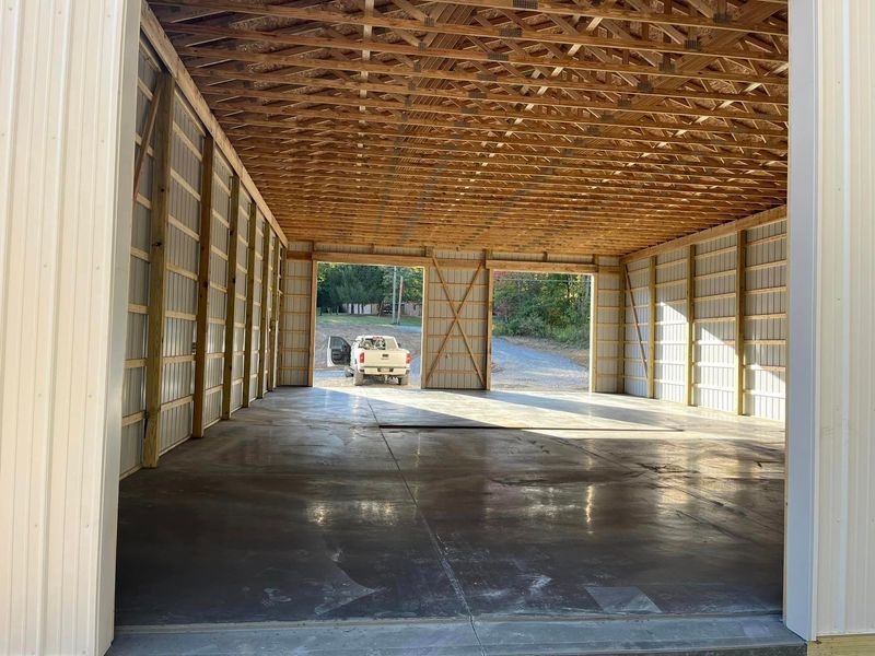 Inside of a large metal building with a concrete floor. Sunlight streams through open doors towards a white truck.