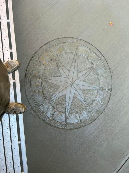 Compass rose design etched into a gray surface, with a partial view of a leg and metal grating.