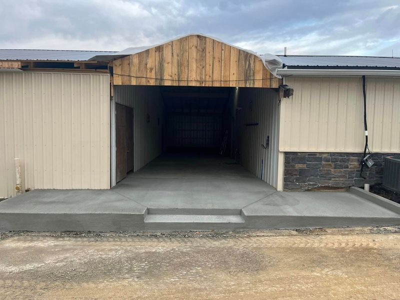 Exterior of a building with concrete ramp and steps leading to a dark opening under wooden arch.