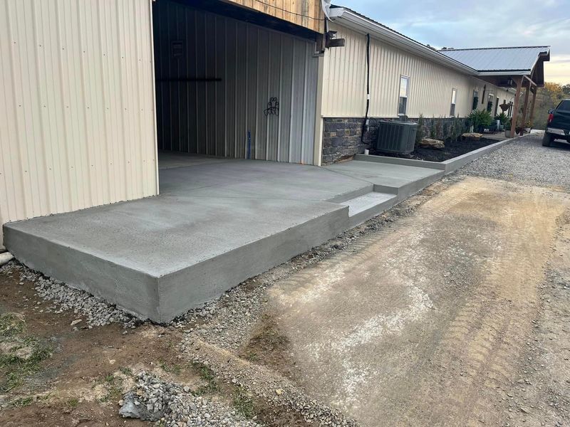 Concrete ramp and step leading to a building with a garage door, gravel driveway.
