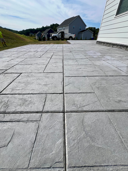 Gray concrete patio with stone pattern, in front of a house under a blue sky.