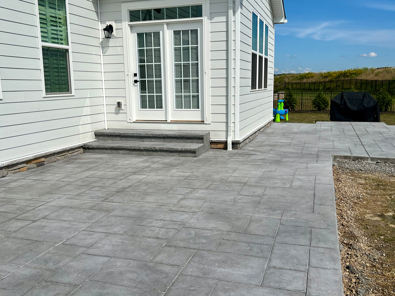 Gray paver patio outside a white house with French doors, steps, and a grill.