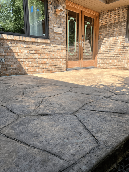 Stamped concrete patio with flagstone pattern, leading to a doorway with glass panes. Brick wall.