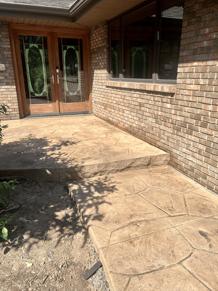 Concrete porch and steps leading to a home's front door, featuring textured stone pattern in shades of tan and brown.