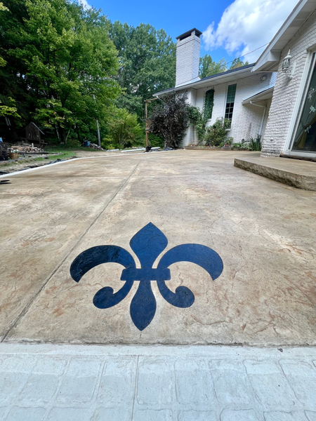 Concrete patio with a blue fleur-de-lis design. A white house and trees are in the background.