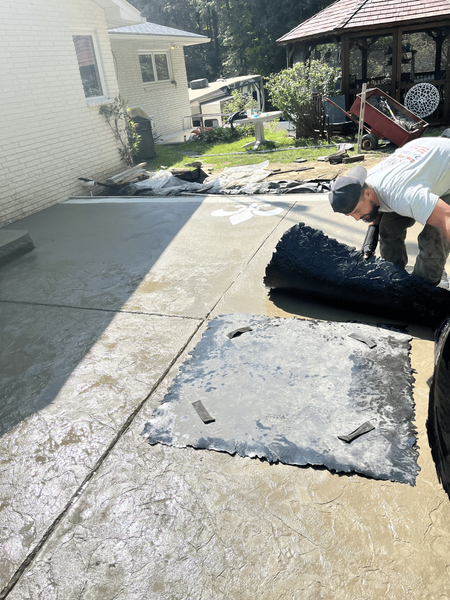 Man stamping decorative pattern onto wet concrete patio near a house and gazebo.