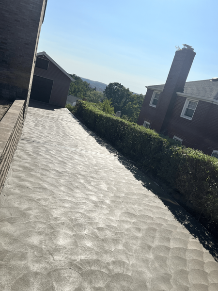 Newly poured concrete driveway, lined with a hedge and brick wall, leading to a distant building on a sunny day.