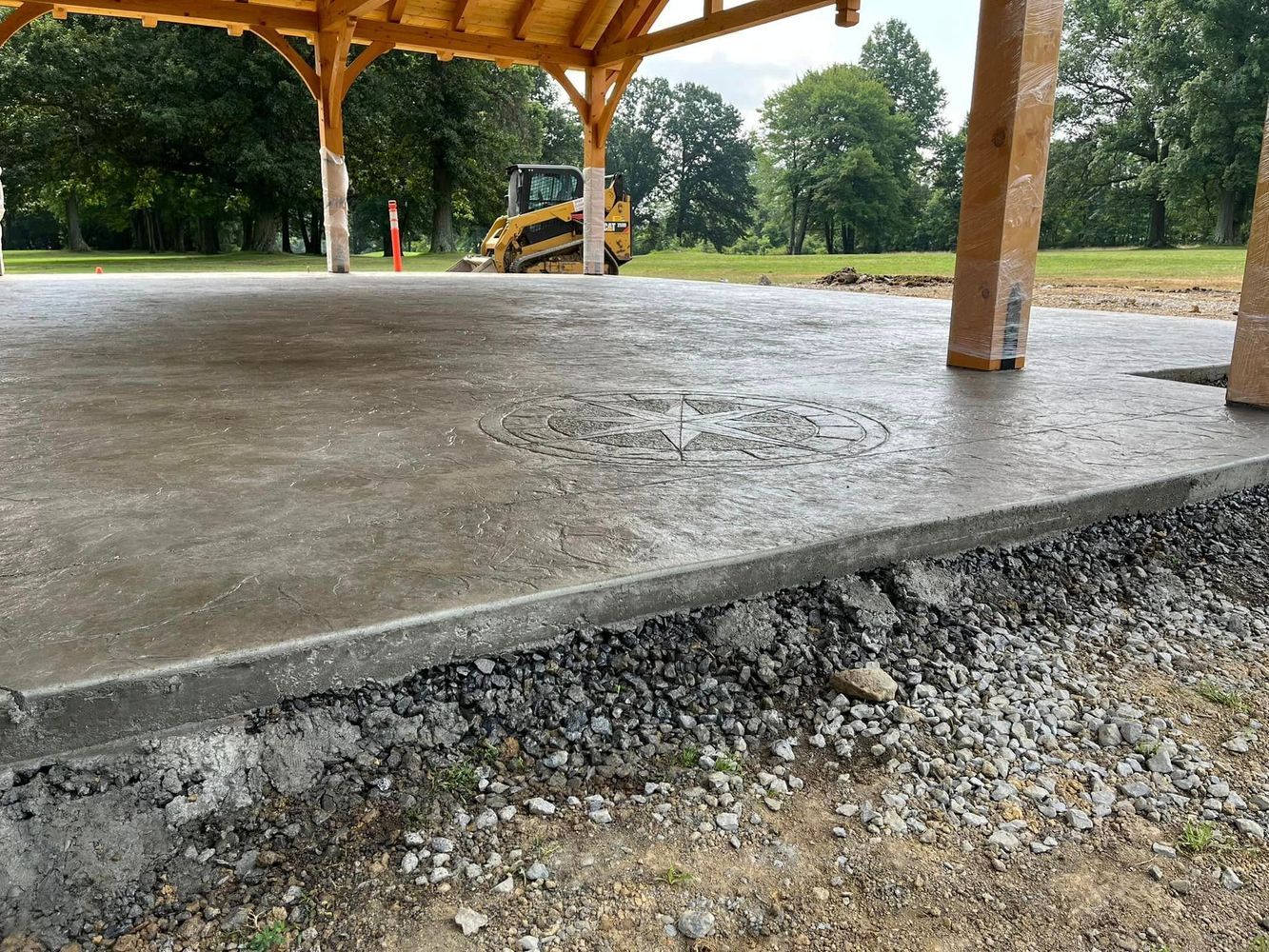 Newly poured concrete floor under a wooden pavilion with gravel border.