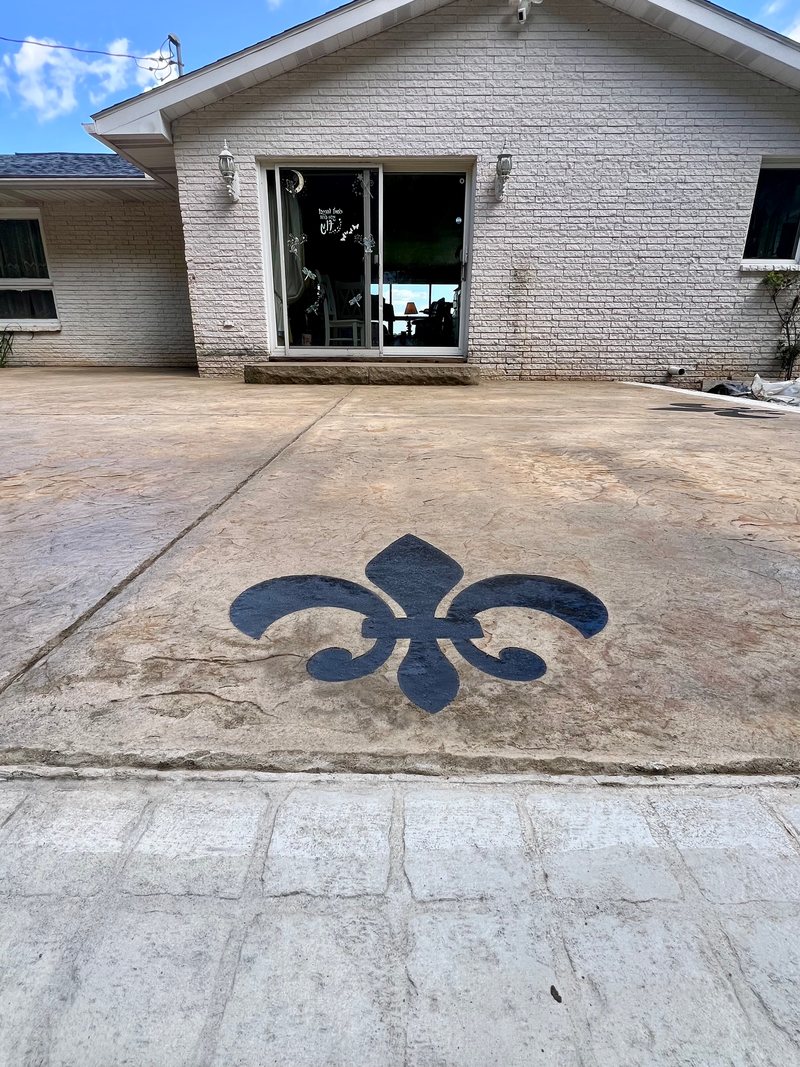 Concrete patio with a black fleur-de-lis design in front of a white brick house with sliding glass doors.