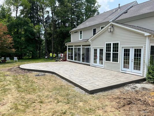 Backyard patio with gray pavers and concrete border; beige house with glass walls and French doors.