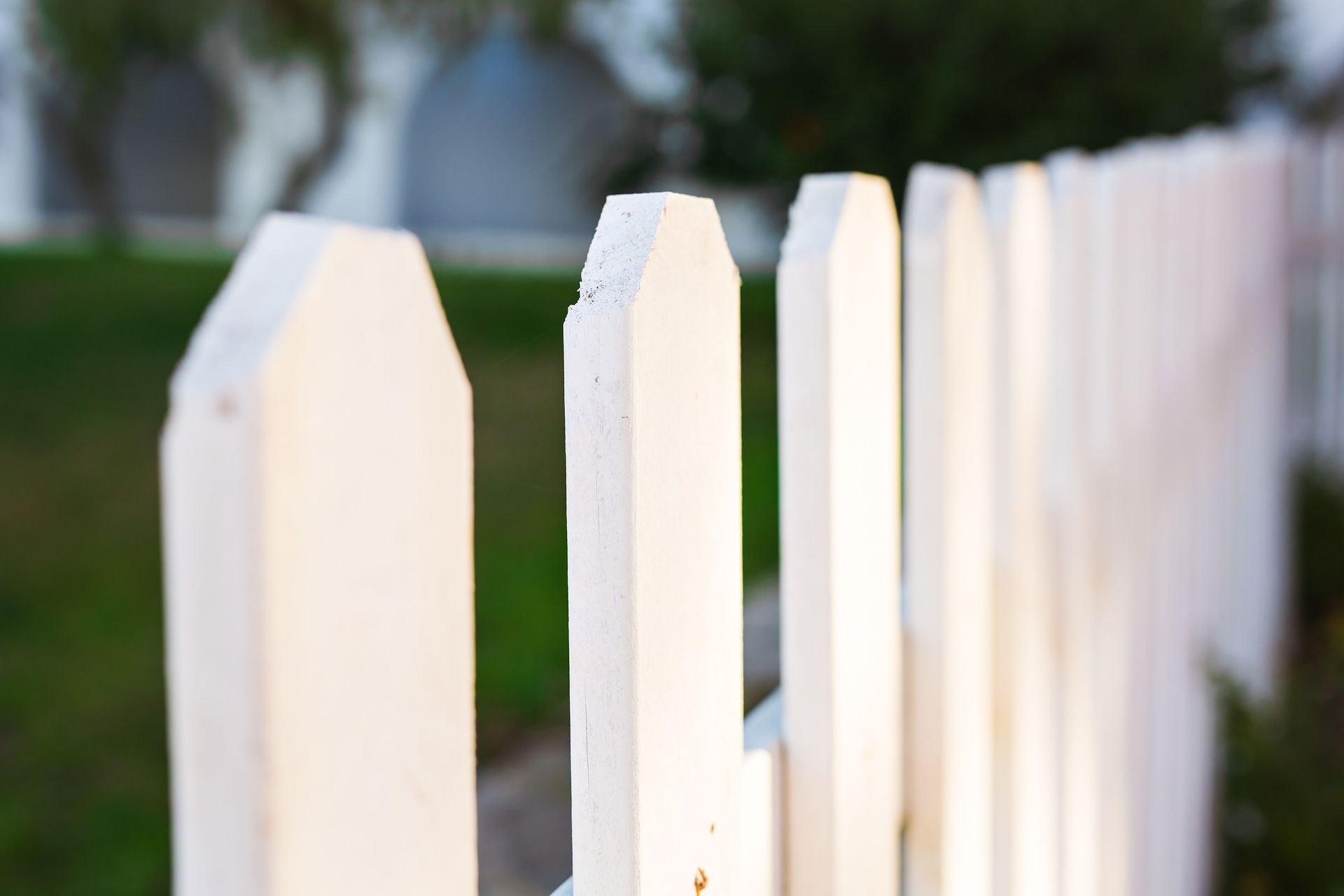 White picket fence, close-up shot with green grass and blurred background.