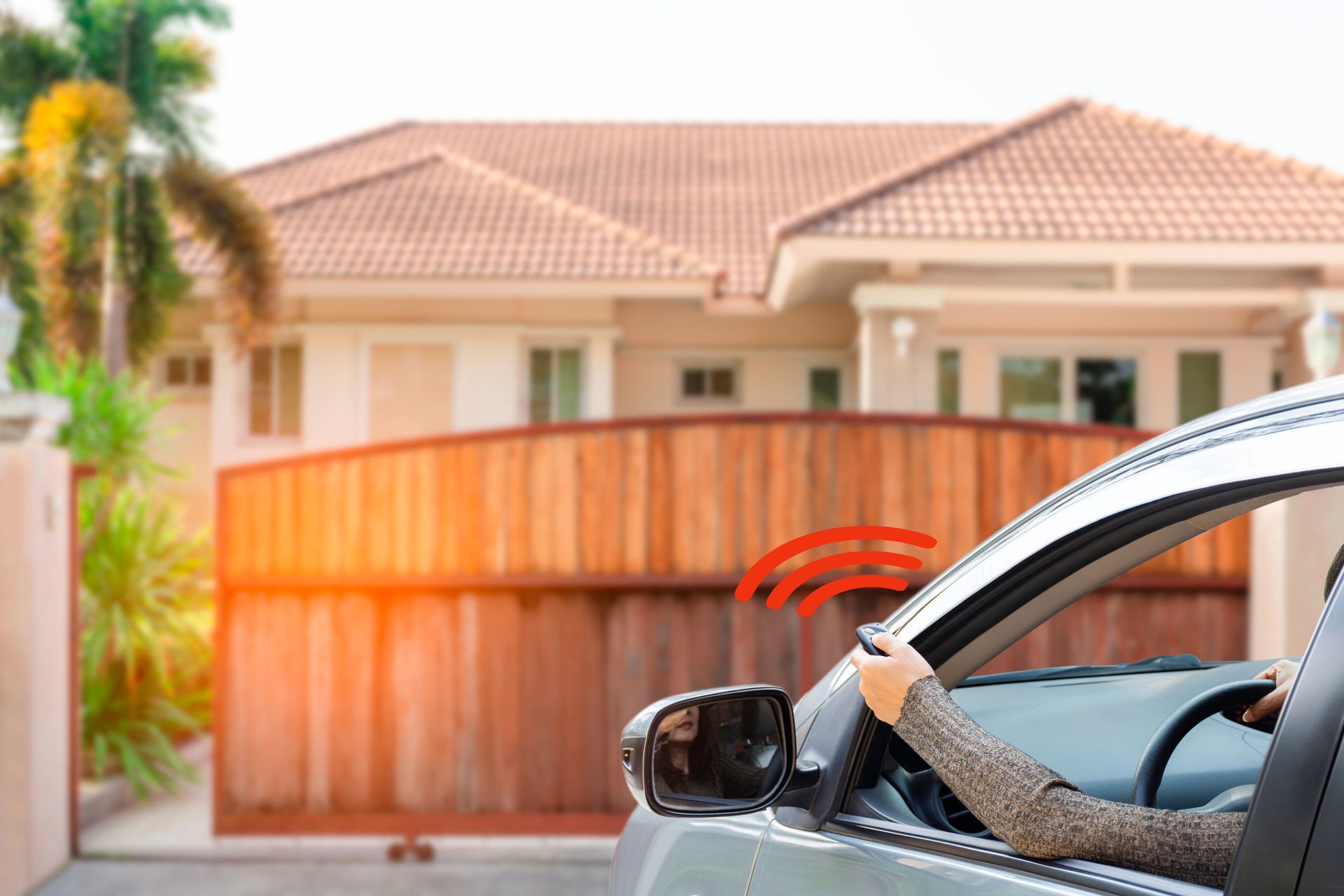 Person in a car using a remote to open a wooden gate to enter a house.