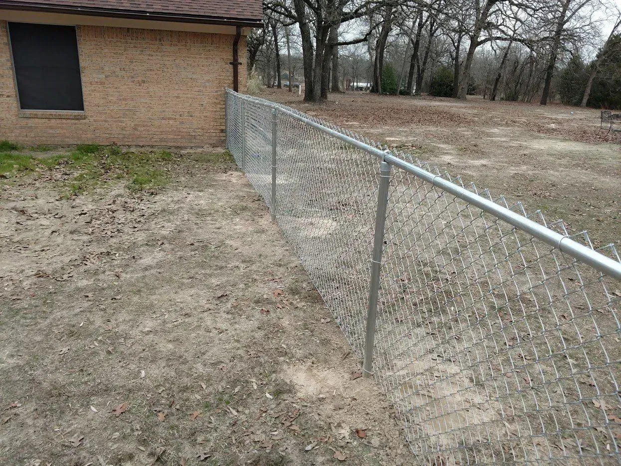 Chain-link fence along the side of a brick building and yard with bare trees.