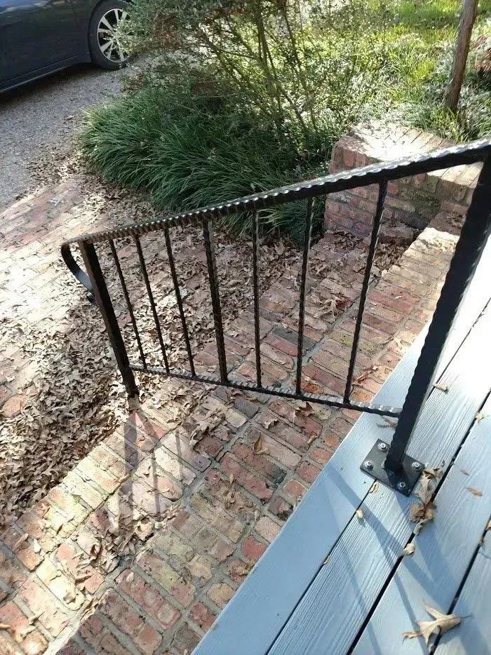 Black metal handrail on brick steps leading to a porch with blue flooring.