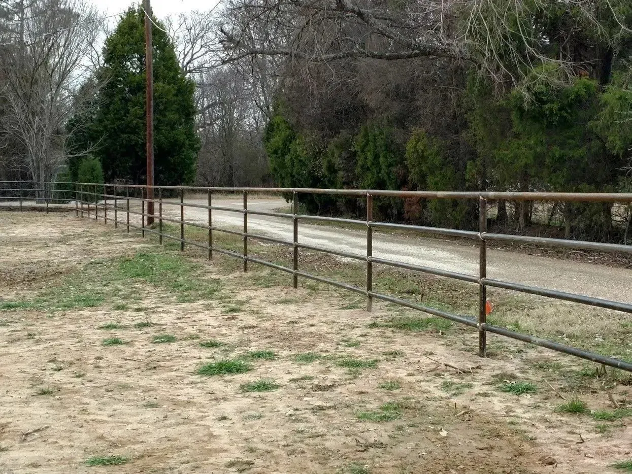 Metal fence bordering a gravel road in a rural setting, with trees in the background.