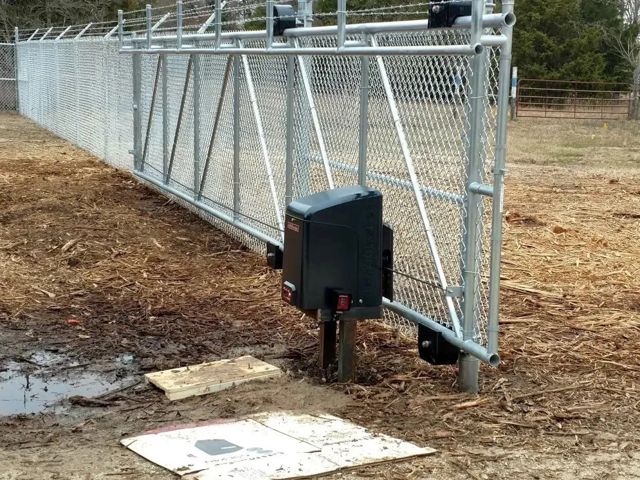 Chain-link fence with an automatic gate opener, set in a muddy field.