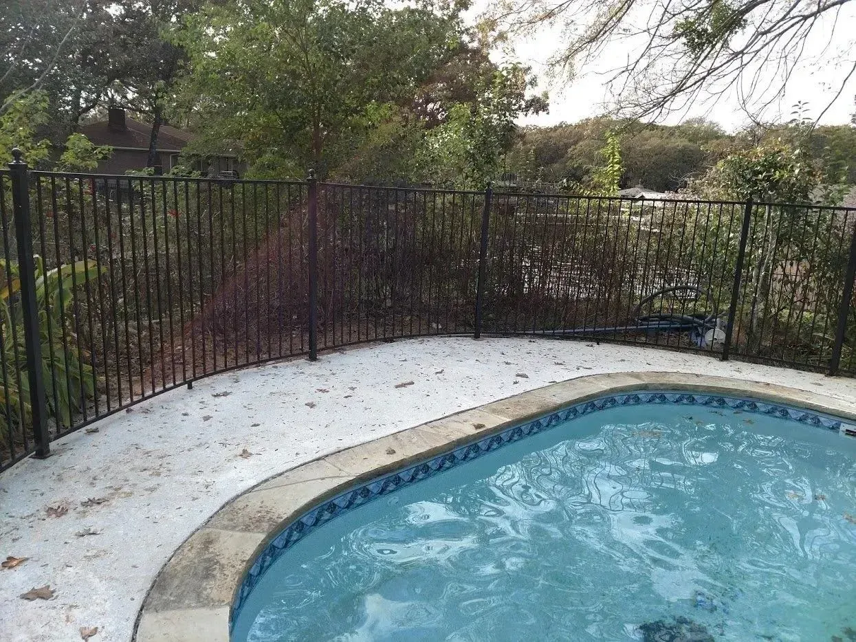 Pool with blue tile, edged with stone and a black metal fence in the background.