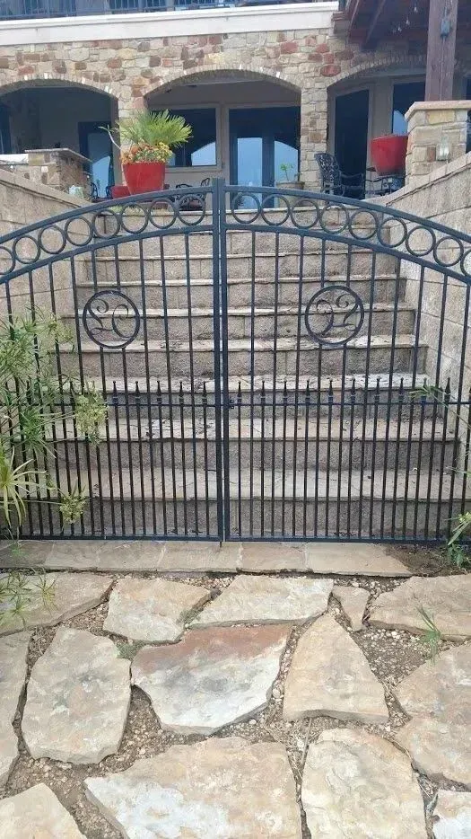 Wrought iron gate on stone steps leading to a house with arched doorways; stone patio in foreground.