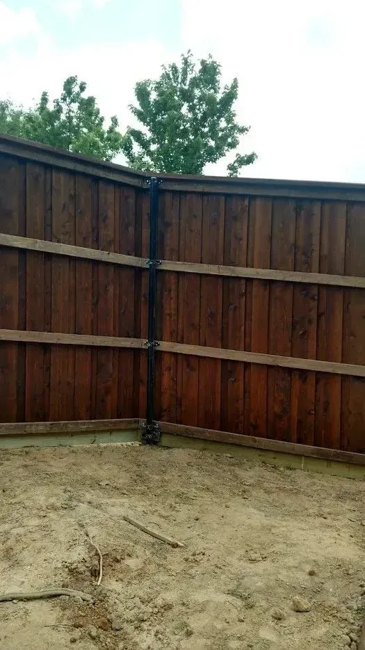 Brown wooden fence with a black pipe attached, set in a yard with dirt.