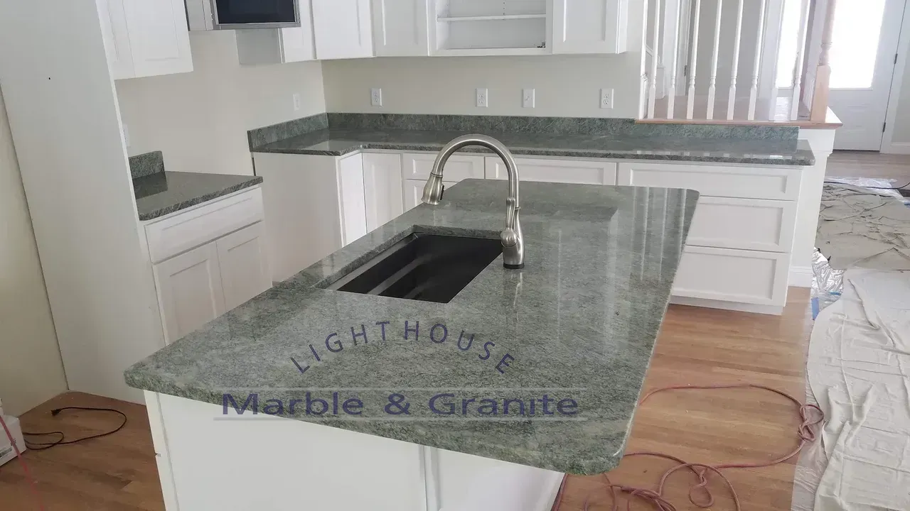 Kitchen with white cabinets and green granite countertops. Island with sink and faucet.