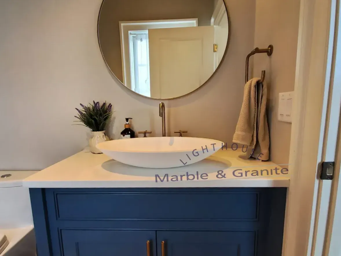 Bathroom vanity with a blue cabinet, white countertop, and vessel sink; a round mirror hangs above.