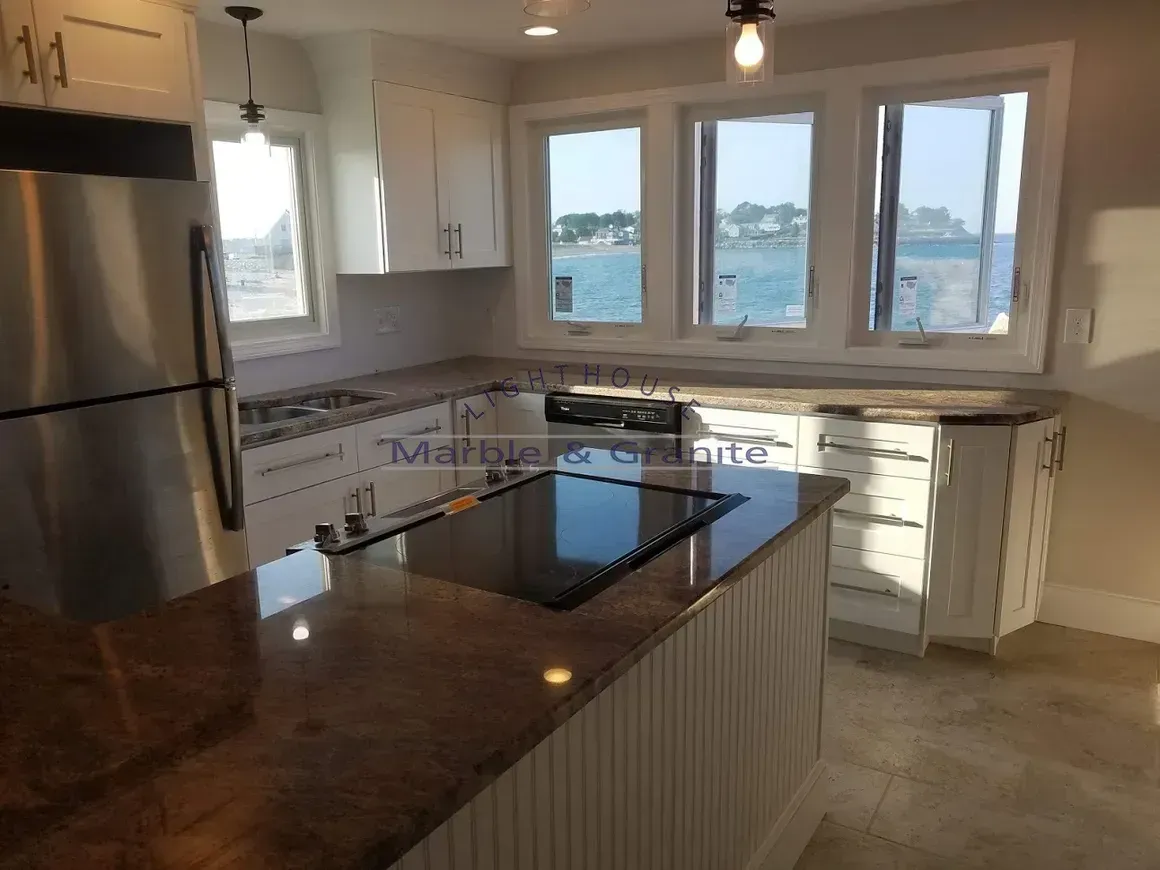 Kitchen with white cabinets, island, and windows overlooking water. Stainless steel appliances and granite countertops.