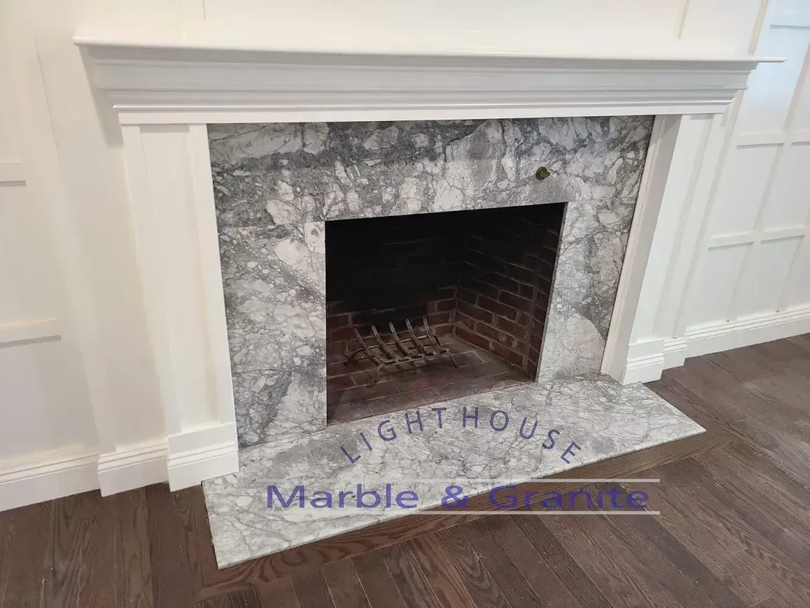 Fireplace with white mantle and gray marble surround, brick firebox, on dark wood floor.