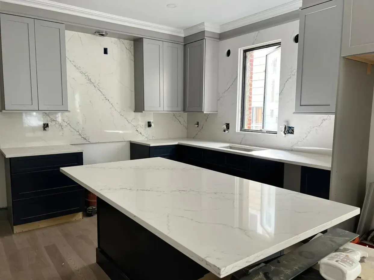 Kitchen remodel in progress: white countertops and backsplash, gray cabinets, dark blue base cabinets, island, and unfinished window.