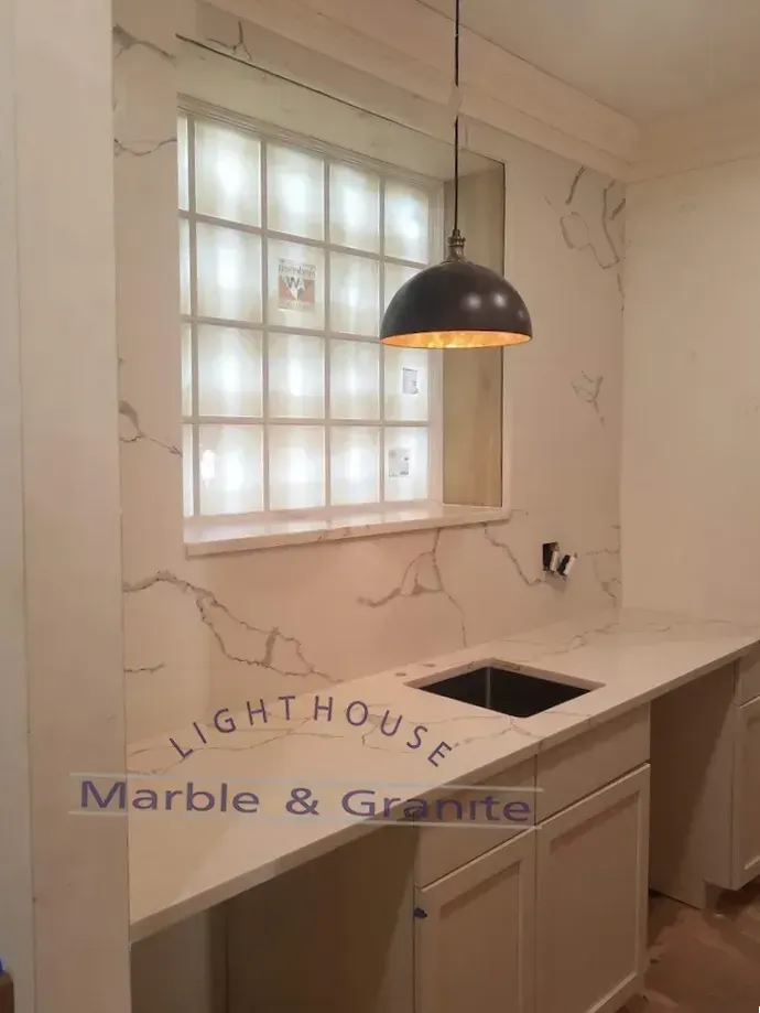 A kitchen countertop with a sink, cabinets, a glass block window, and a hanging light fixture.
