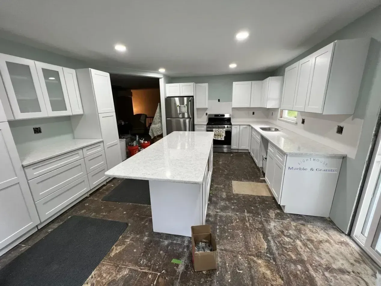 White kitchen with island and cabinetry; unfinished floor, stainless steel appliances.