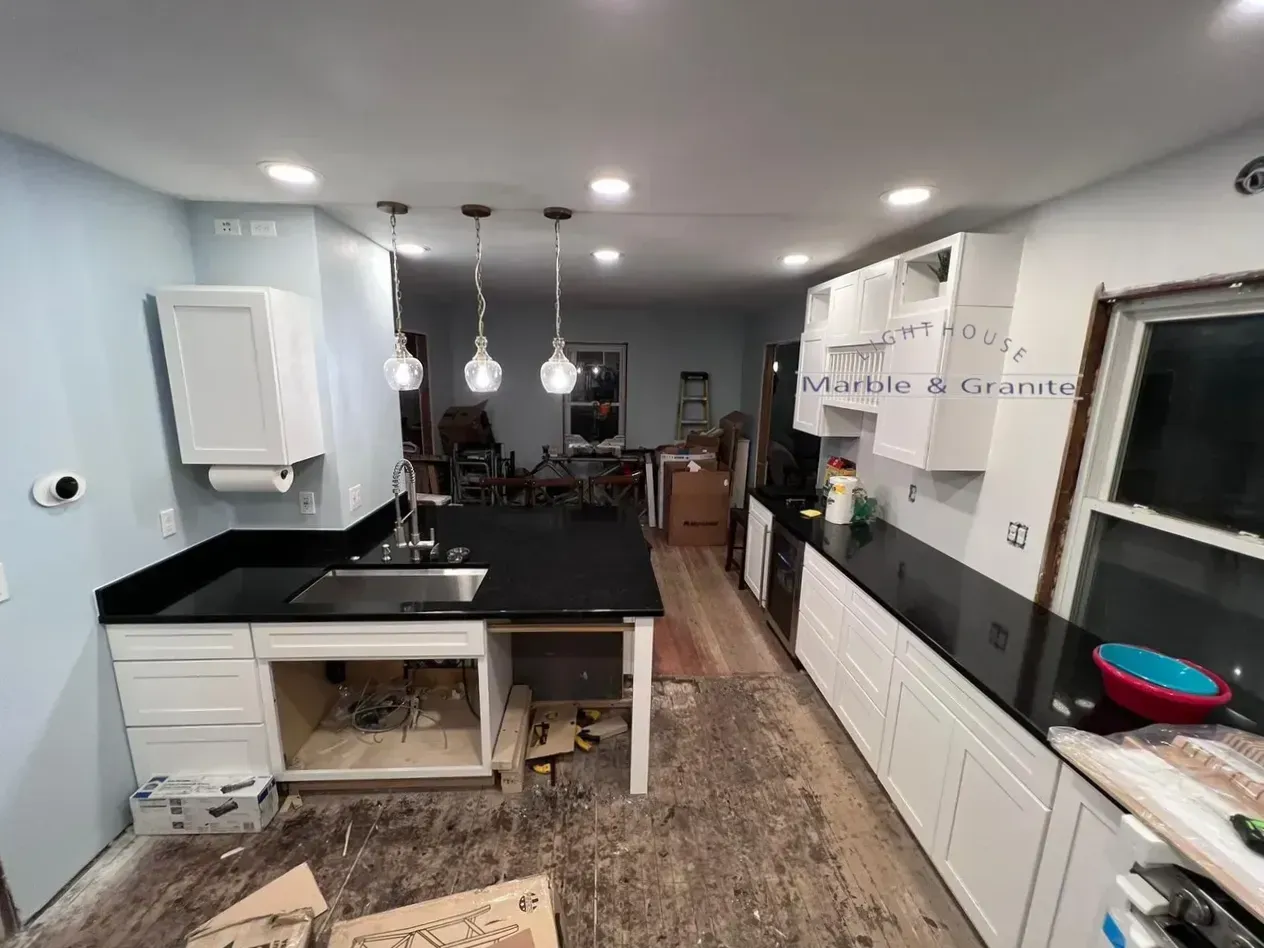 Kitchen under renovation with black countertops, white cabinets, and wooden flooring.
