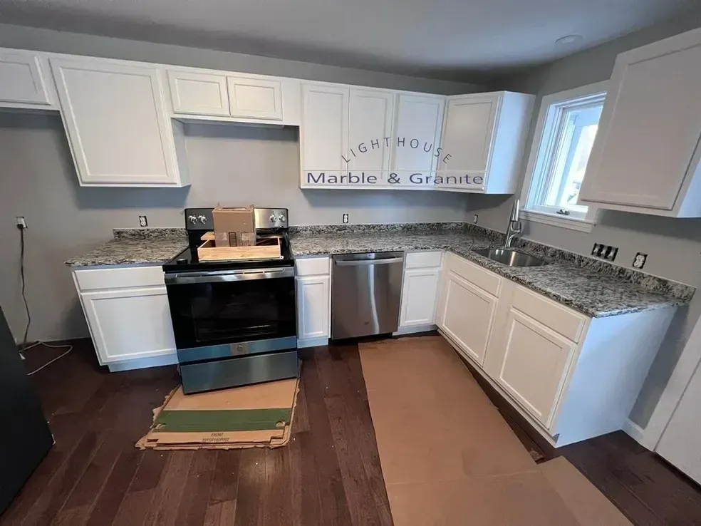 White kitchen cabinets with granite countertops, stainless steel appliances, and dark hardwood floors.
