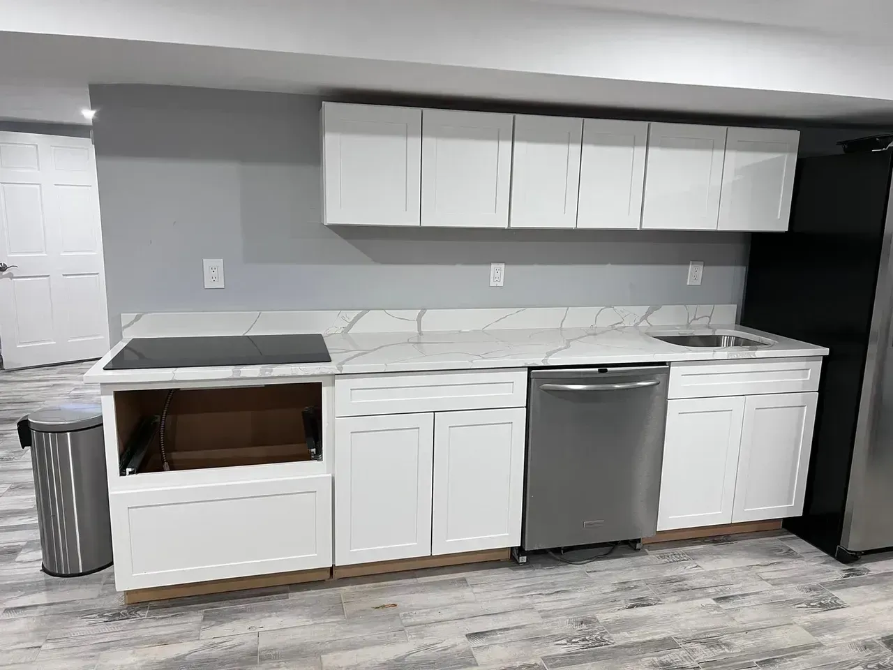 White kitchen cabinets with gray countertops and stainless steel appliances in a basement setting.
