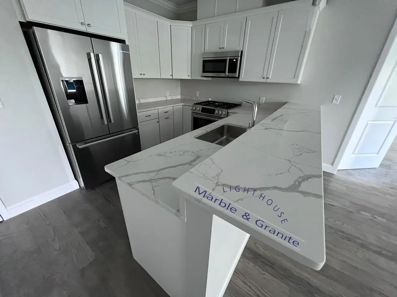 White kitchen with marble countertops, stainless steel appliances, and cabinets.