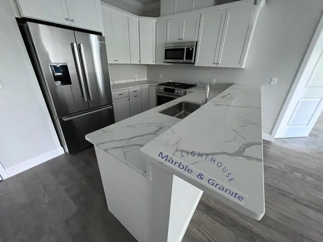 White kitchen with marble countertops, stainless steel appliances, and cabinets.