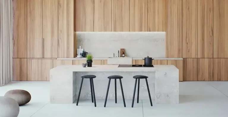 Modern kitchen with light wood paneling, a stone island with black stools, and cooking appliances.